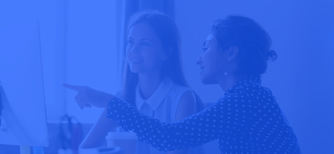 Woman showing a younger colleague how to do a task on the computer, with a blue tone overlay.